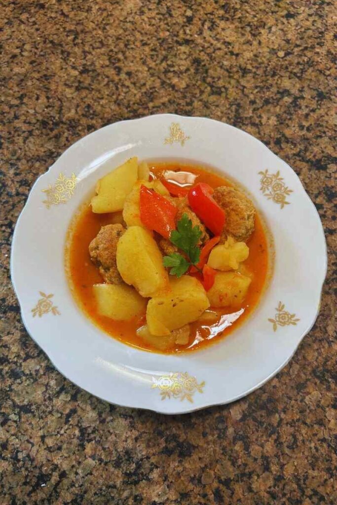 Close-up of hearty Italian meatballs and potatoes in rich tomato sauce, garnished with parsley, served as a comforting one-pot meal.