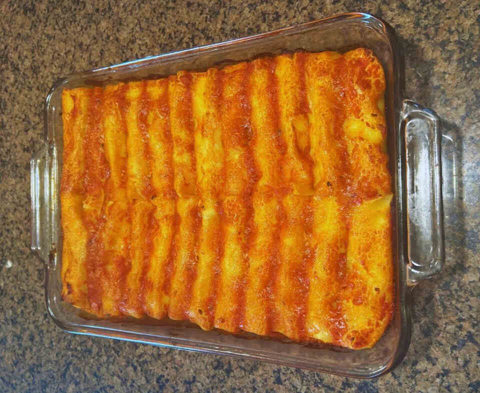 Ricotta and mozzarella cannelloni baking in a tray, covered with tomato sauce and melted cheese.