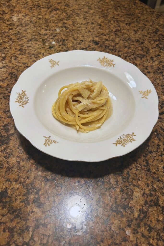 A plate of Cacio e Pepe topped with grated pecorino Romano cheese and cracked black pepper, with the pasta coated in a creamy, glossy sauce.