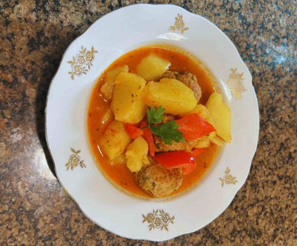 Plate of homemade meatballs and tender potato chunks cooked in savory tomato sauce.