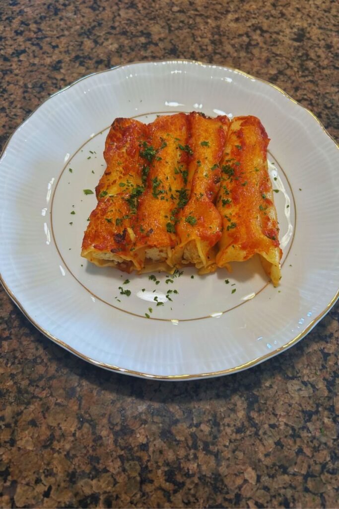 Golden baked ricotta and mozzarella cannelloni topped with tomato sauce and melted cheese on a plate.