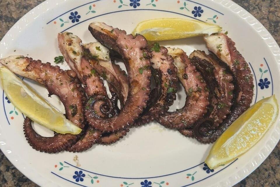 A close-up shot of a platter with Grilled Octopus with Garlic, Lemon Zest, Herbs & Peppercorns