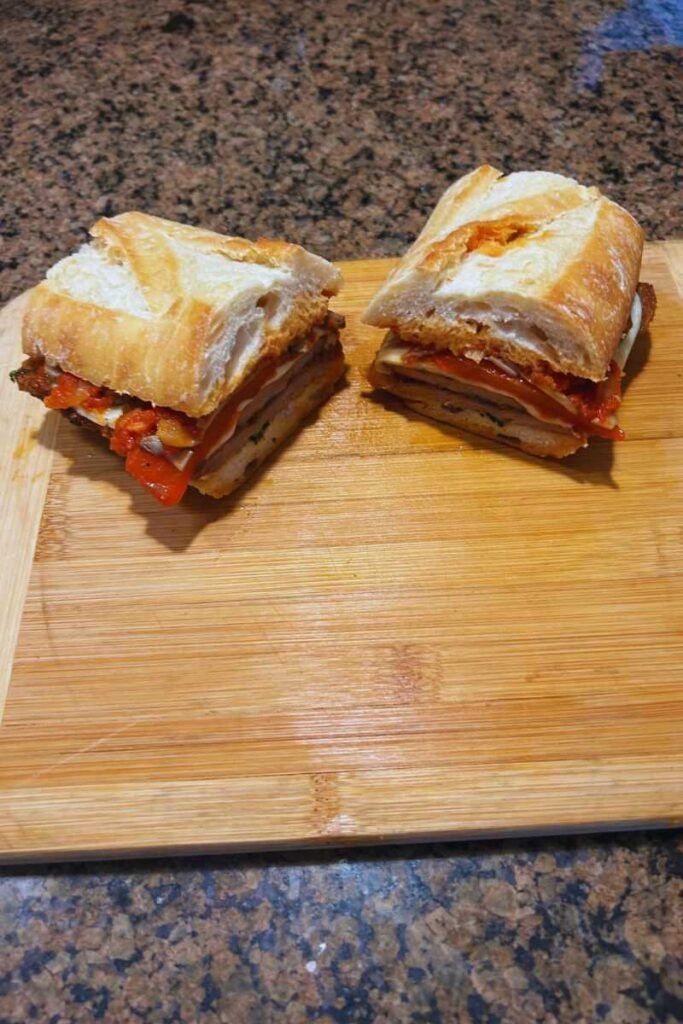 An Italian Breaded Beef Cutlet Sandwich cut in half on a cutting board.