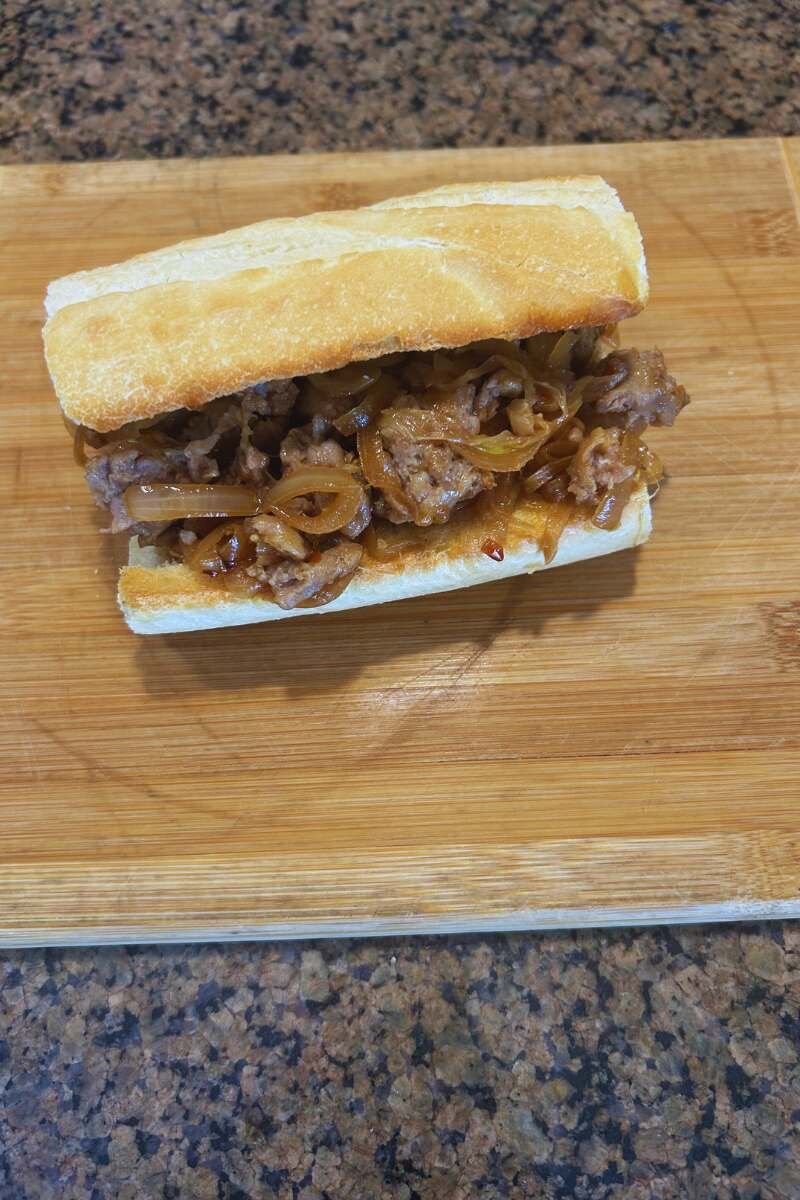 An Italian Fennel Sausage Ciabatta with Caramelized Onions on a cutting board.