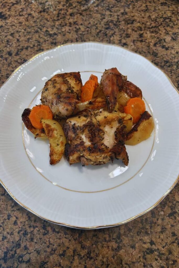 A plate of Oven Roasted Rabbit with Potatoes and Vegetables on a countertop.