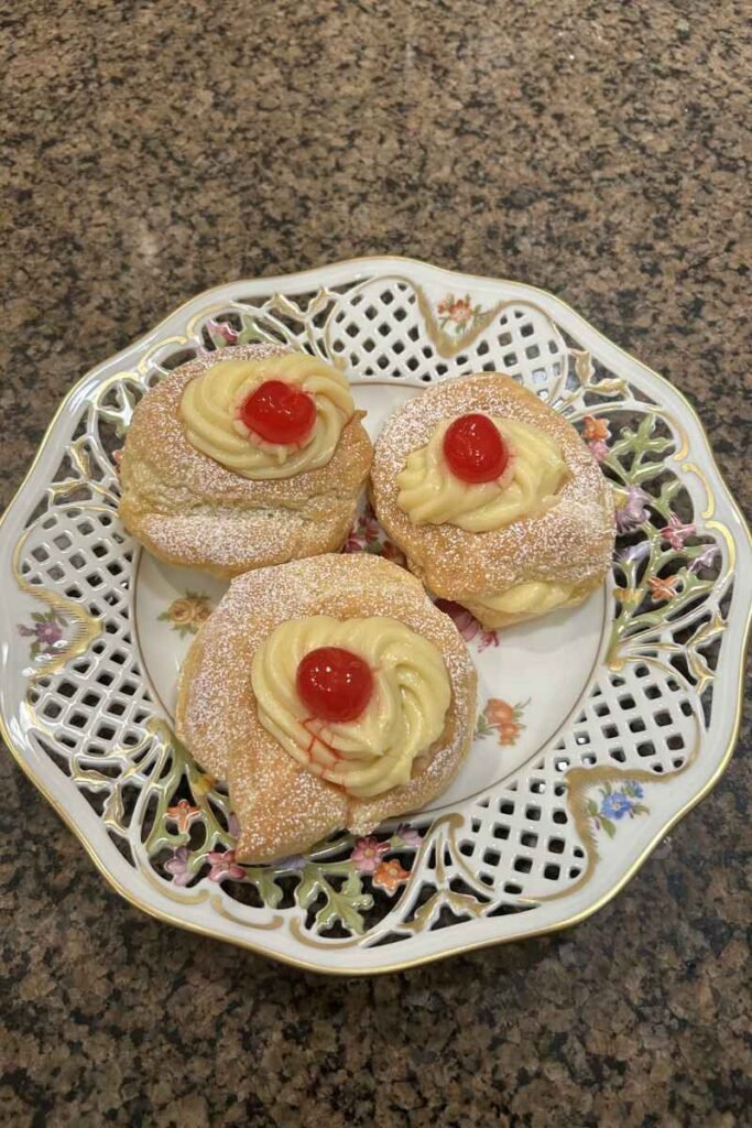 A plate with three zeppole di san giuseppe, on the countertop.