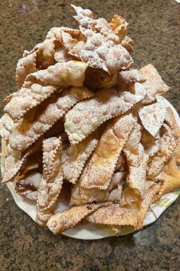Freshly fried Italian crostoli dusted with powdered sugar cooling on a kitchen countertop.