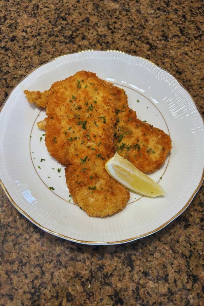 A plate with chicken cutlets and a lemon wedge, placed on a countertop.